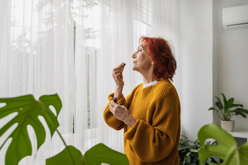 Retired senior woman smelling essential oil from bottle at home