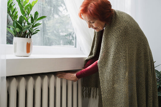 Senior woman examining temperature of radiator at home