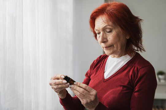 Retired senior woman reading label on essential oil bottle at home