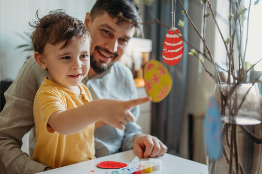 Happy father with son touching cardboard Easter eggs on twigs