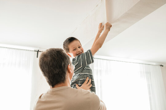 Happy boy helping father in peeling old wallpaper from wall at home