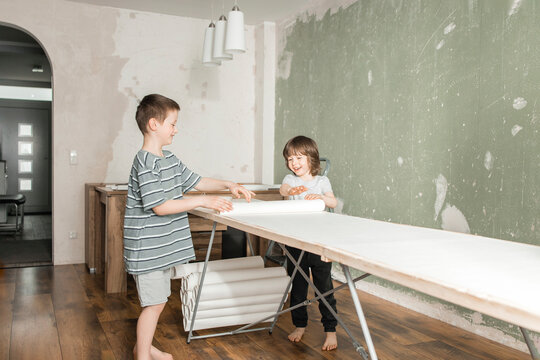 Happy brothers rolling out wallpaper on construction table at home