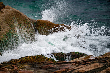 Powerful waves crash against rugged boulders and stones, creating dynamic spectacle of nature raw force. tumultuous sea surges, sending salty spray into air, as waves collide with coastal formations