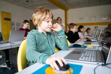 Blond boy learning computer coding through laptop in classroom