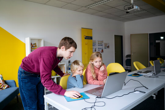 Teenage boy assisting students with coding in classroom