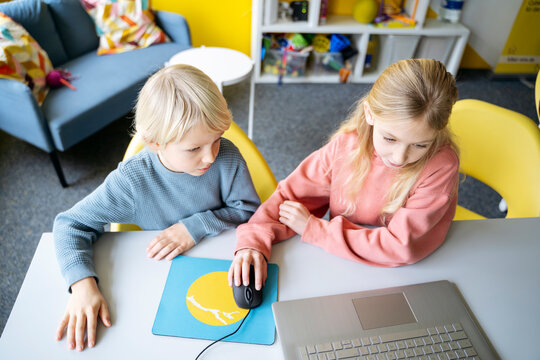 Girl and boy sharing laptop for learning computer coding in classroom