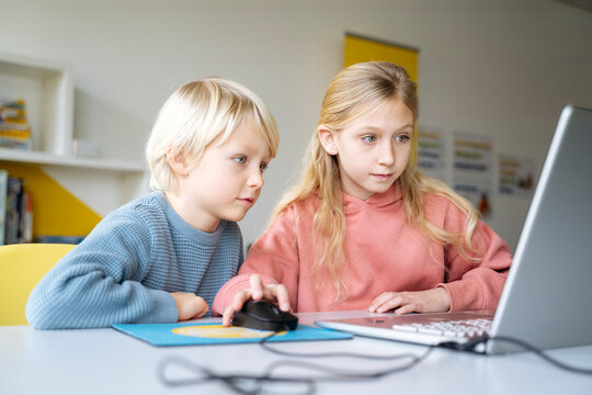 Girl and boy sharing laptop for learning computer coding in school classroom