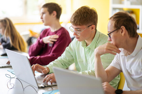 Teenage boy using laptop by professor in classroom