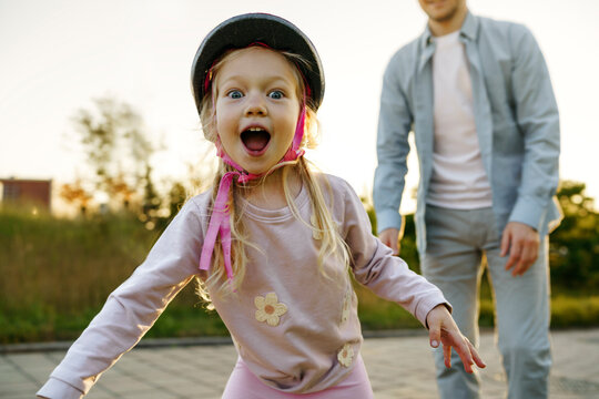 Cheerful girl wearing sports helmet with father in background