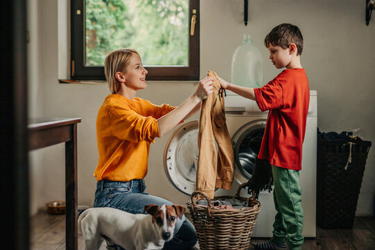 Mother and son doing laundry together in utility room at home