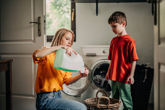 Mother pouring detergent near son standing by washing machine at home