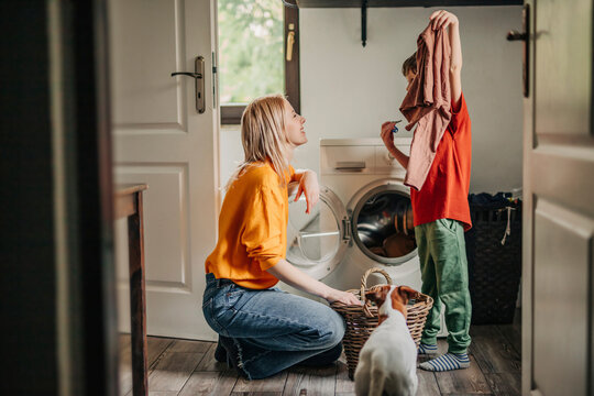 Son showing washed clothes to mother crouching near washing machine at home