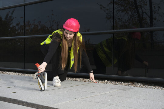 Young geodesist measuring floor width with tape near building