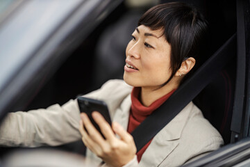 A middle aged japanese woman is driving her car and using a cellphone.