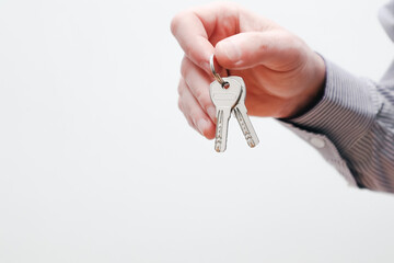 Hand holding house keys. Moving house, relocation. Caucasian male hand holding key to house on white background. Copy space