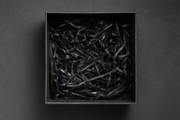 Black gift box with shredded paper on a black background. top view