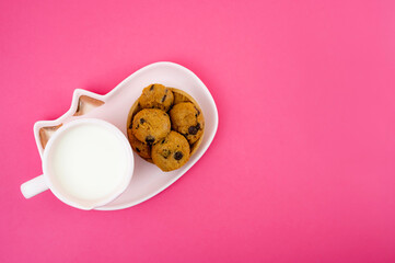 Obraz na płótnie Canvas Chocolate chips cookies served on a small wooden bowl with a cup of milk, isolated on pink background. A close-up and selective focus photo of the cookie. A top view photo. A copy space.