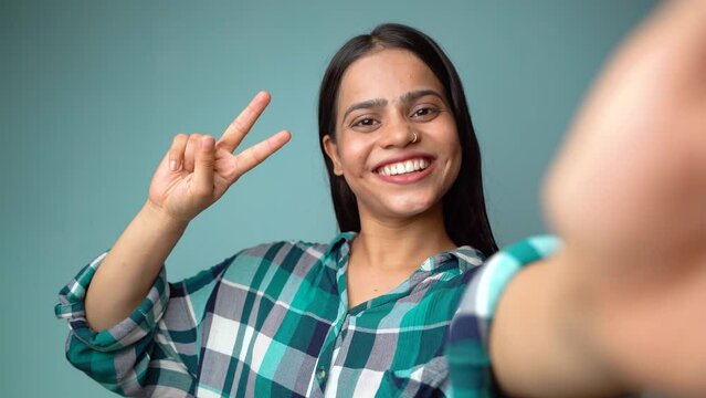 Young woman taking selfie portrait, POV shot of a beautiful Asian Indian girl taking her picture and showing peace sign or v-sign