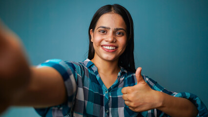 Young woman taking selfie portrait, POV shot of a beautiful Asian Indian girl taking her picture and showing thumbs up gesture - obrazy, fototapety, plakaty