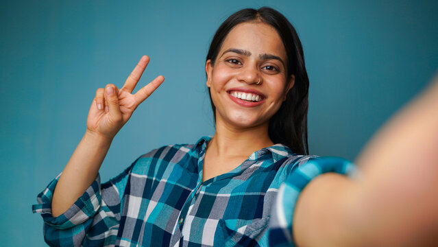 Young woman taking selfie portrait, POV shot of a beautiful Asian Indian girl taking her picture and showing peace sign or v-sign