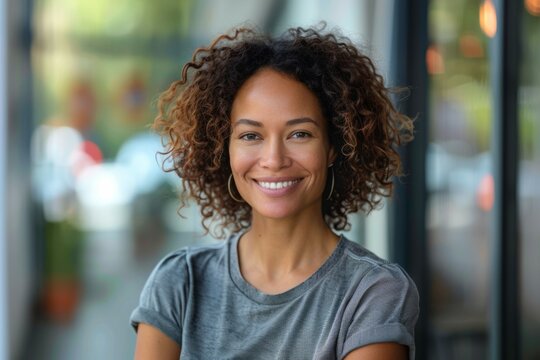 A woman with curly hair is smiling and wearing a gray shirt
