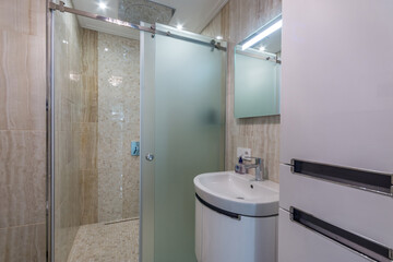The bathroom is decorated with beige tiles. Shower cabin with frosted glass door.