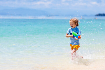 Child with toy water gun. Kids vacation beach fun.
