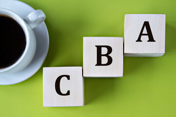 CBA - acronym on wooden big cubes on green background with cup of coffee