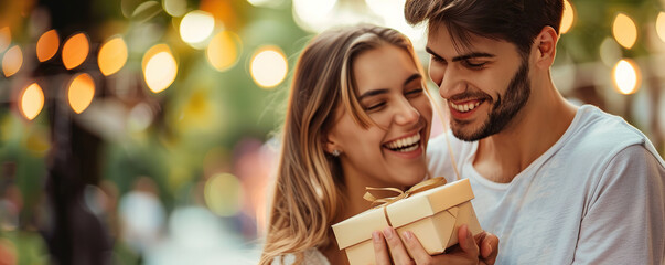 A man and a woman are holding a gift for each other. They are smiling and seem happy