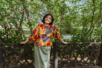 Joyful young woman in colorful blouse enjoying a sunny day in the park. Stylish asian woman enjoying a summer day while walking in a green park