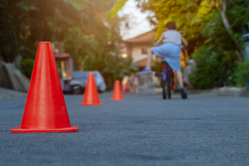 Focus to orange traffic cones on street with blurry group of children learn to riding bicycle in...