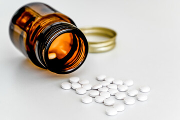 White Pills Scattered on Table Next to Brown Glass Vial, on White Background, Close-up