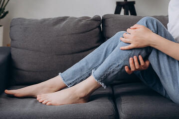 Close up of young woman massaging brawn leg calf muscle cramps or spasm, trauma from inflammation of tendon at calves while sitting alone on couch at home. Muscle pain or leg pain. Health care concept