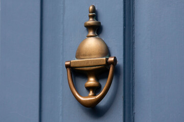 Close-up of old fashioned gold door knocker against chalk blue door 