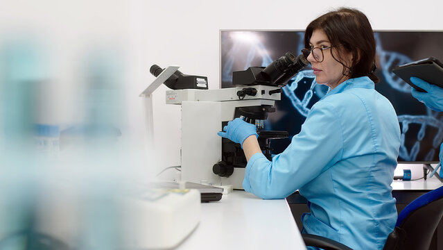 Medical scientific laboratory. Professional biotechnologist developing drugs. A female biochemist working at a computer with an image of genetic research in the background.