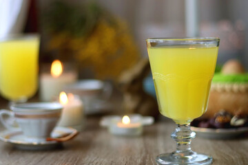 Easter eggs in the basket, bowl of cookies, chocolate pralines, Easter bunny figurine, cups of tea, glasses of juice, flowers and lit candles on the table. Selective focus.