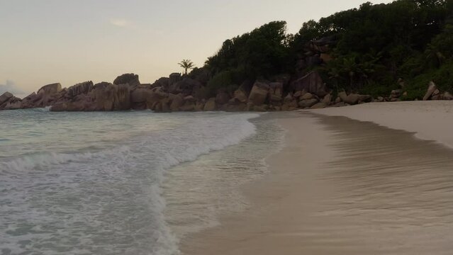Waves crashing onto the sandy beach during sunset. White sandy beach lined with granite boulders in La Digue, Seychelles. Beautiful secluded beach with no people. Empty remote islands. Wavy shoreline