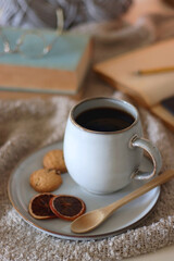Cup of tea or coffee, cookies, books, glasses, e-reader, almonds, ball of yarn, knitting needles and lit candles on the table. Hygge at home. Selective focus.