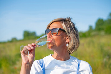 junge Frau mit Sonnenbrille trinkt Sekt auf einer Wiese