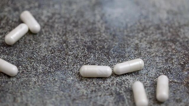White pills fall onto a dark surface. Drugs fall on a dark table. Medical and pharmaceutical business concept. Coronavirus vaccine. Pills.