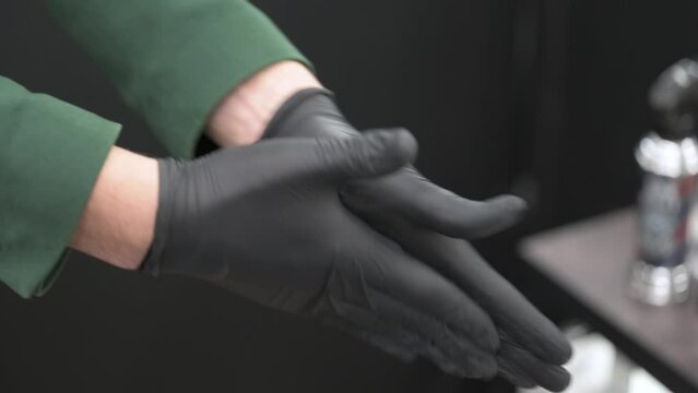 A barber in black gloves rubs wax and pomade for styling a clients hair.