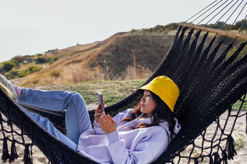A young attractive Asian woman holds a mobile phone and lies in a hammock. A charming Korean woman...