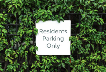 Parking for residents only sign on the fence among leaves of bush