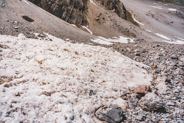 A snow avalanche comes down from the rocky Fan Mountains in Tajikistan, pieces of snow fall like...