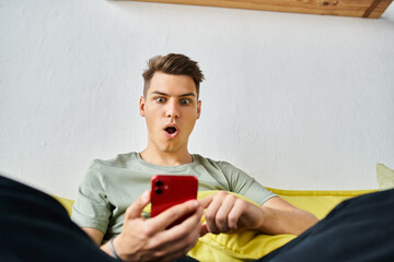 surprised student in his 20s at home sitting on yellow couch and scrolling in social media - 766997847