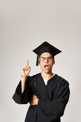 attractive young student in graduate outfit and vision glasses come up to idea on grey background