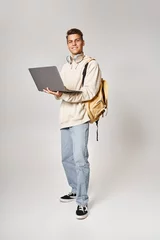 Fototapete Rund young student in headphones standing with backpack and networking to laptop against grey background © LIGHTFIELD STUDIOS