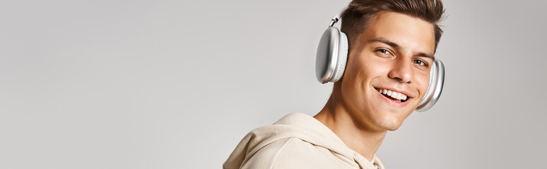 horizontal shot of young guy with brown hair in headphones smiling to camera on light background