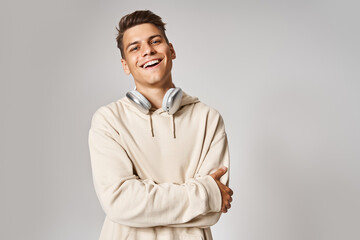 handsome young guy in headphones smiling with folded arms against light background