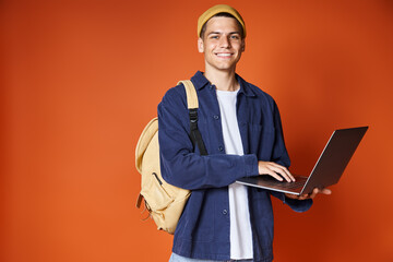 attractive student with backpack networking to laptop against terracotta background